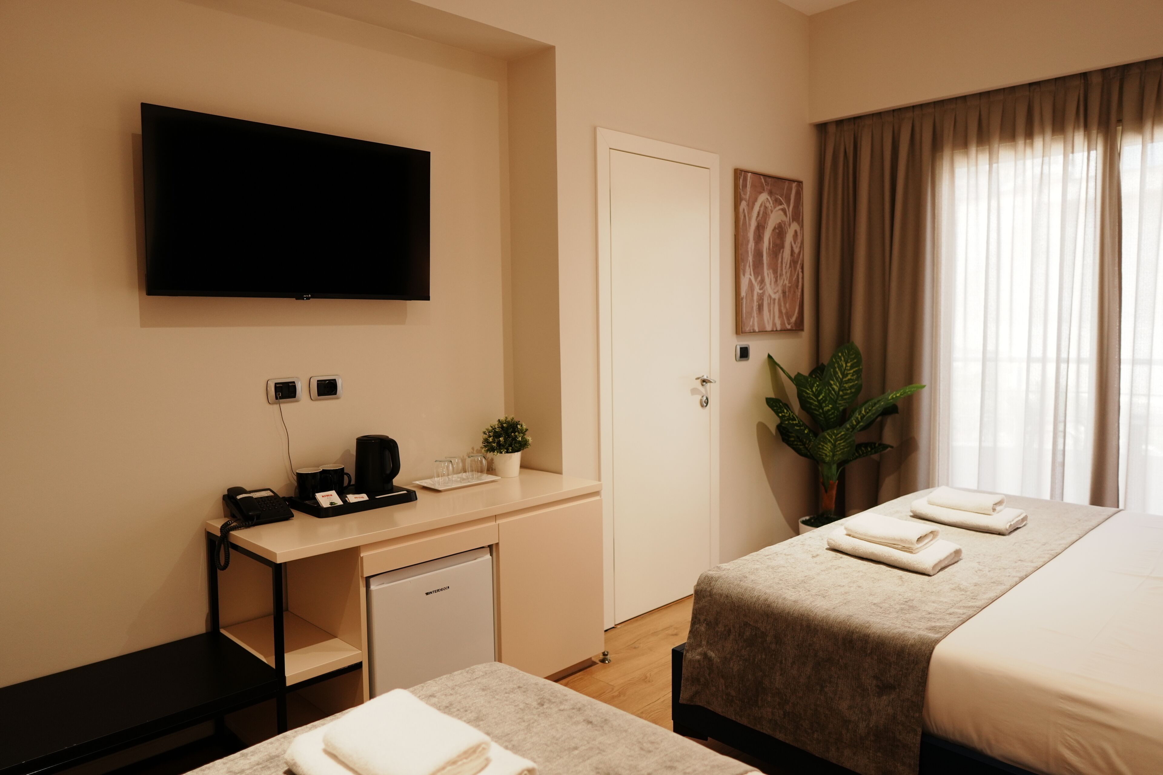 A hotel room with a bed, a desk with a coffee maker, a TV, and a plant.