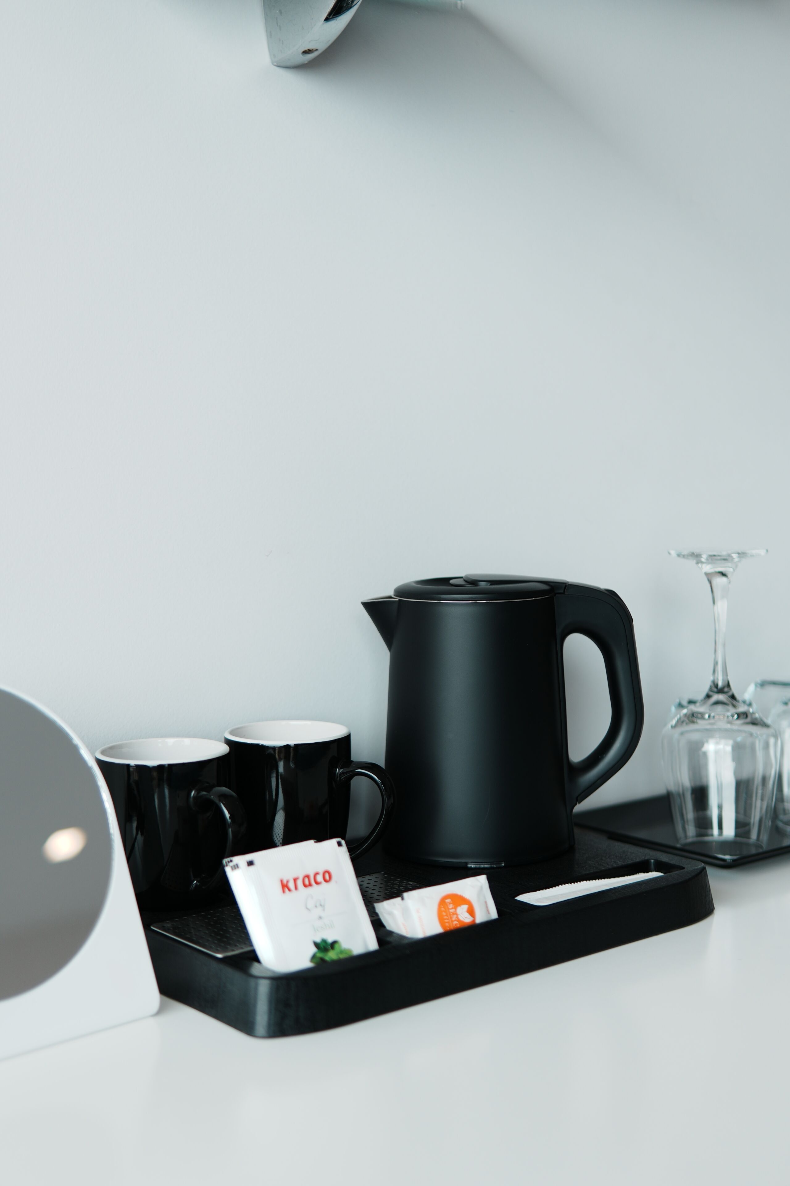 Uma estação de café com uma cafeteira, duas canecas, um copo e uma bandeja com cápsulas de café.