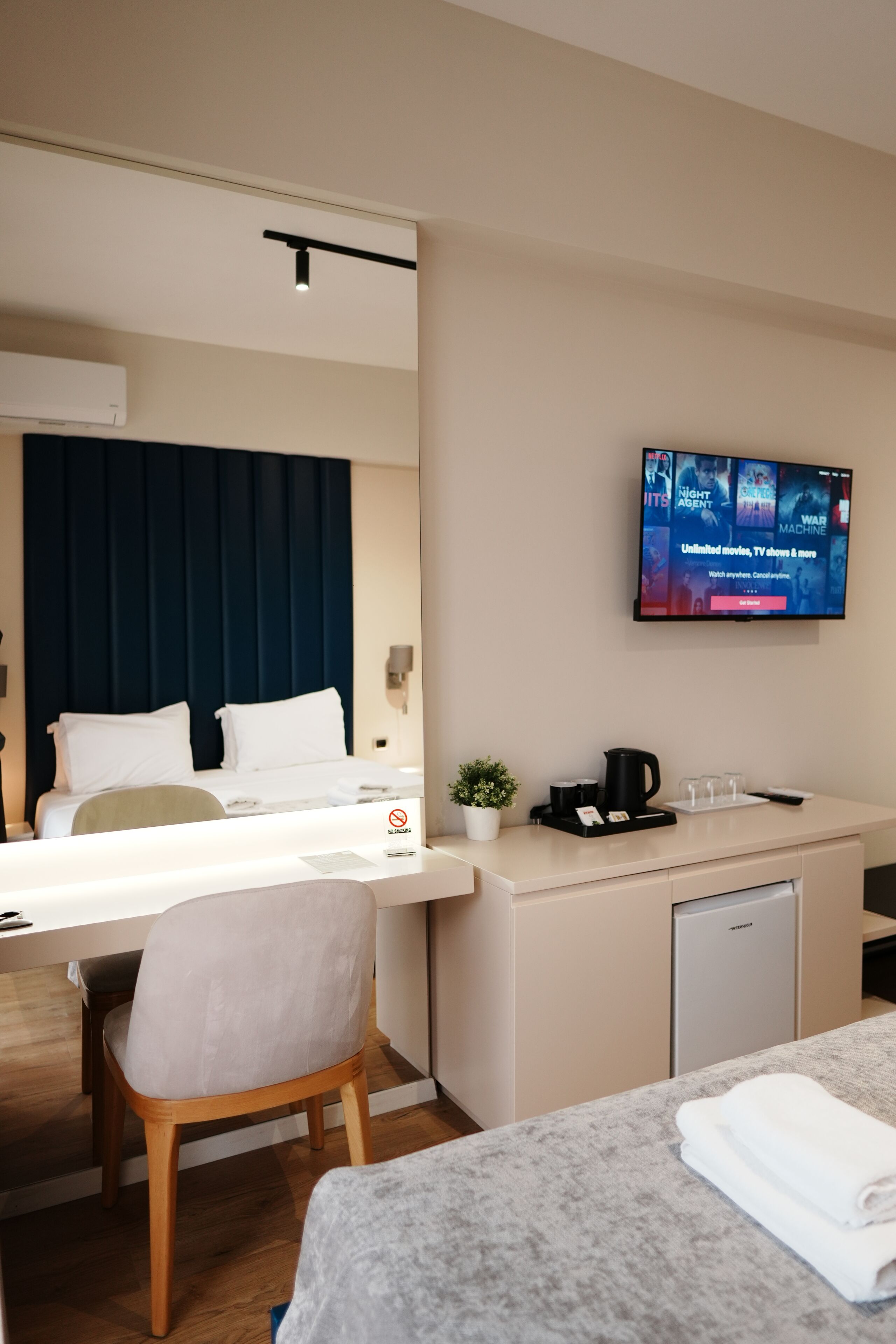 Habitación de hotel con cama, escritorio, silla, televisor montado en la pared y una pequeña zona de kitchenette.