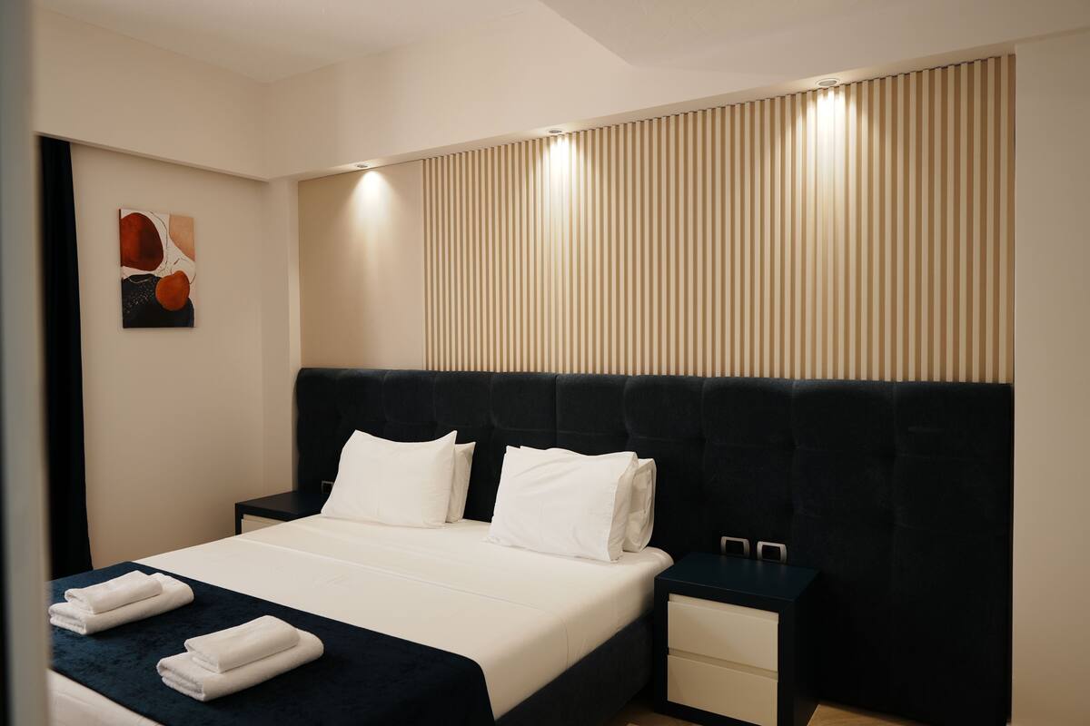 A modern hotel room with a large bed, bedside tables, a headboard, and a wall-mounted artwork.