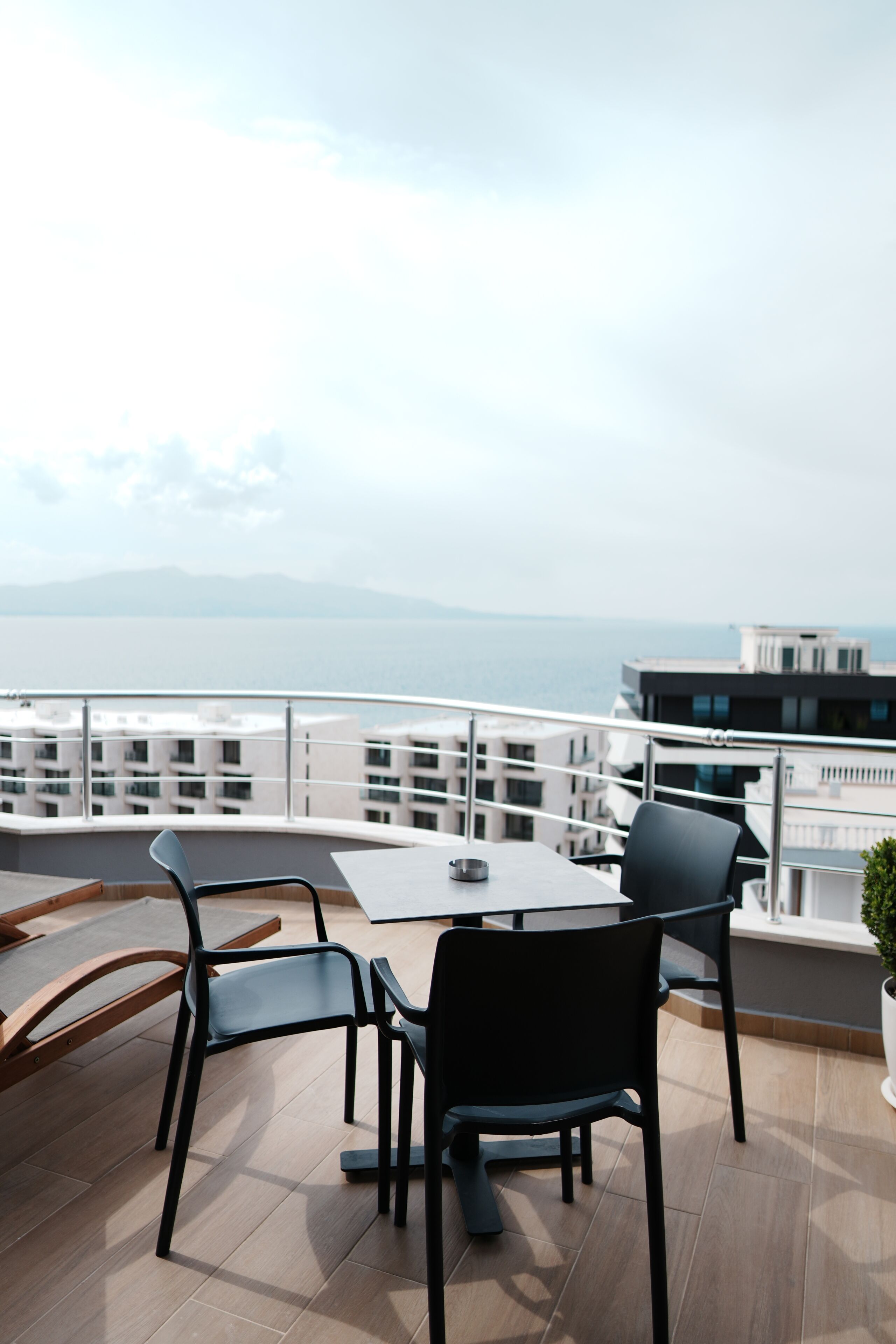 A balcony with a table and chairs, overlooking a body of water and buildings.