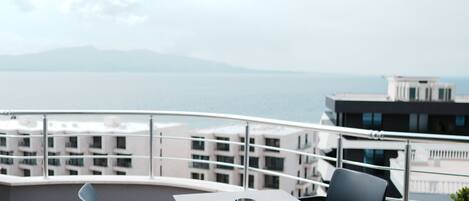 A balcony with a table and chairs, overlooking a body of water and buildings.