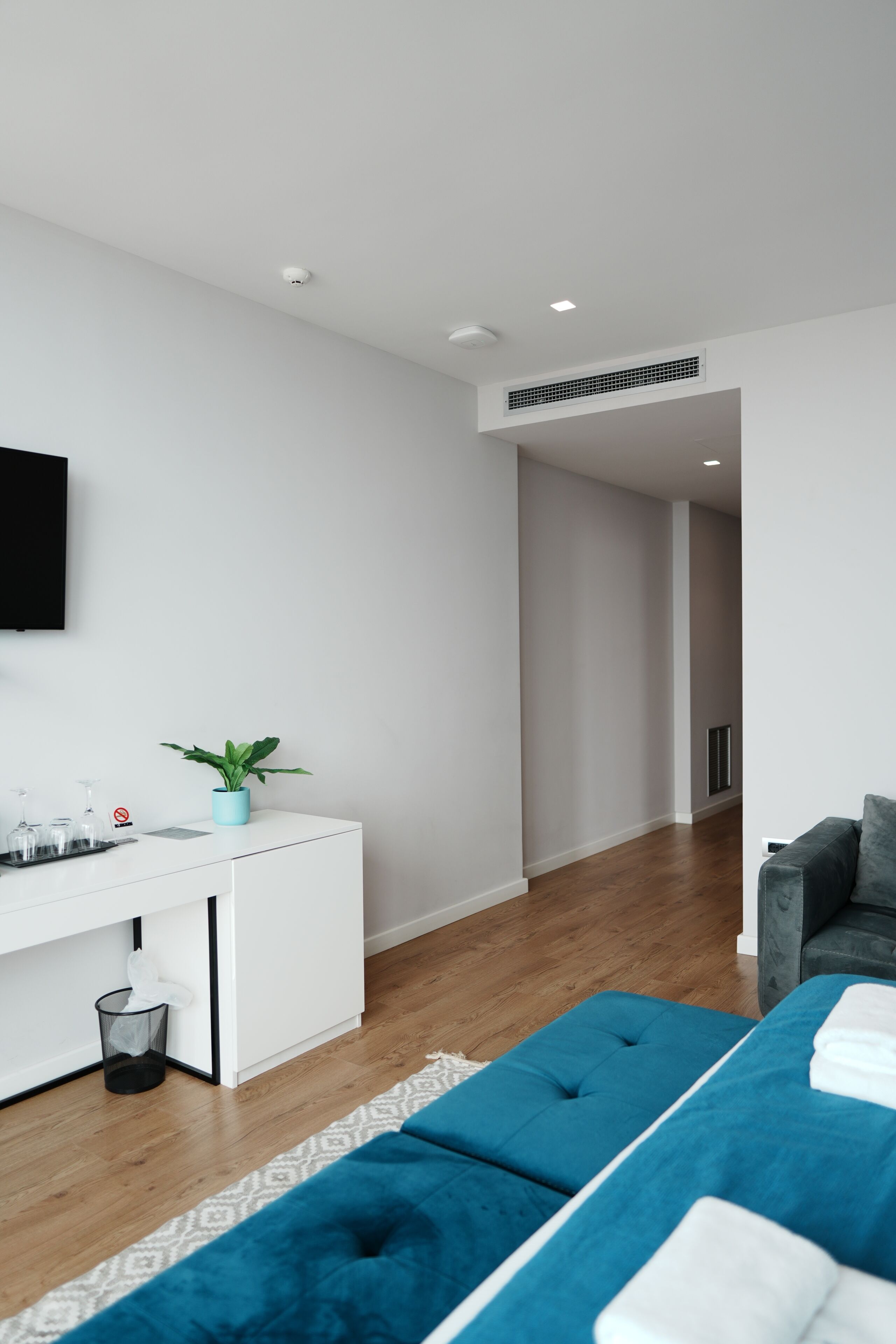 A modern living room with a white desk, a blue potted plant, a grey sofa, and a blue ottoman.