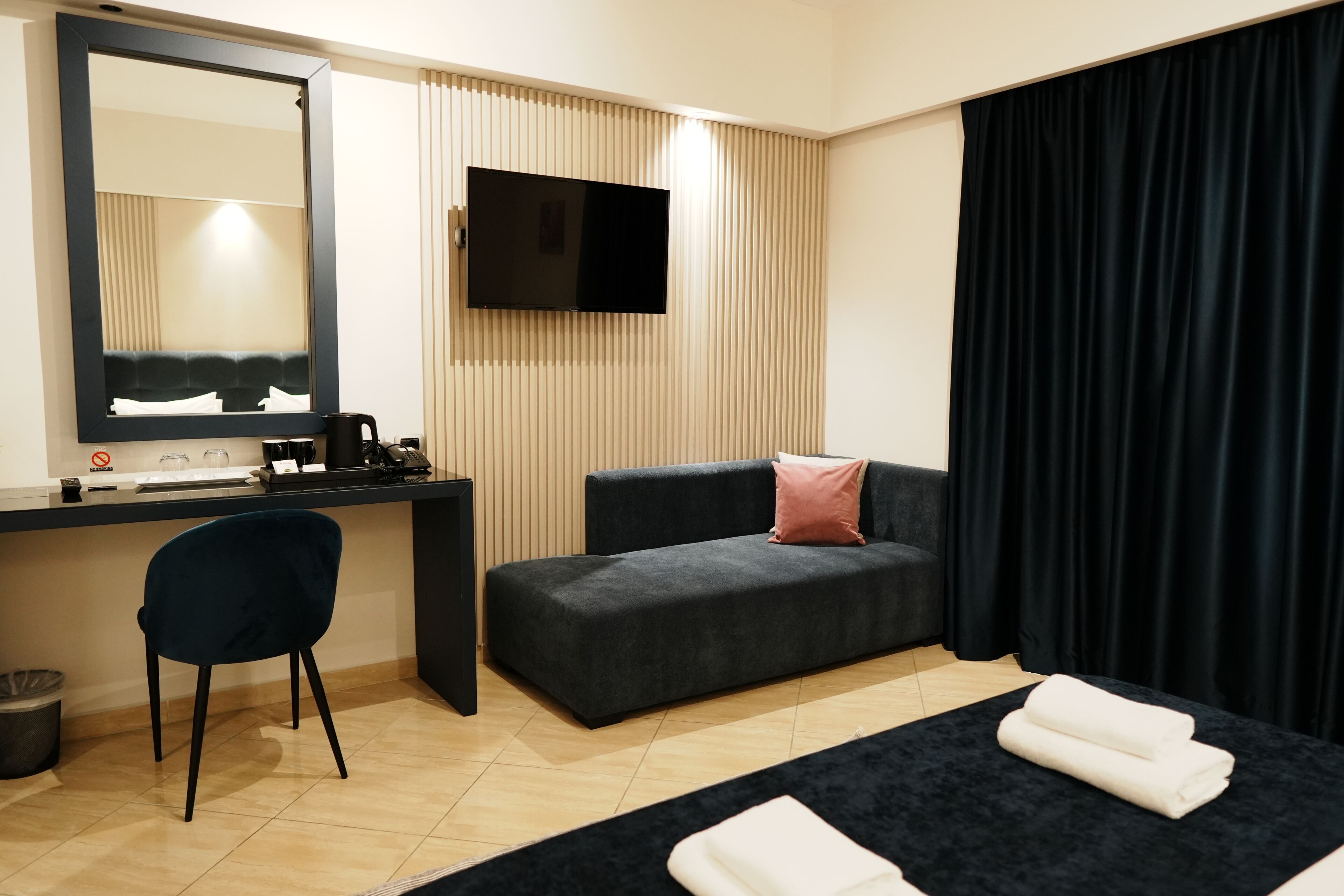Habitación de hotel con escritorio, televisor de pantalla plana, sofá, silla y cama con toallas.