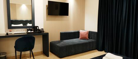 Habitación de hotel con escritorio, televisor de pantalla plana, sofá, silla y cama con toallas.