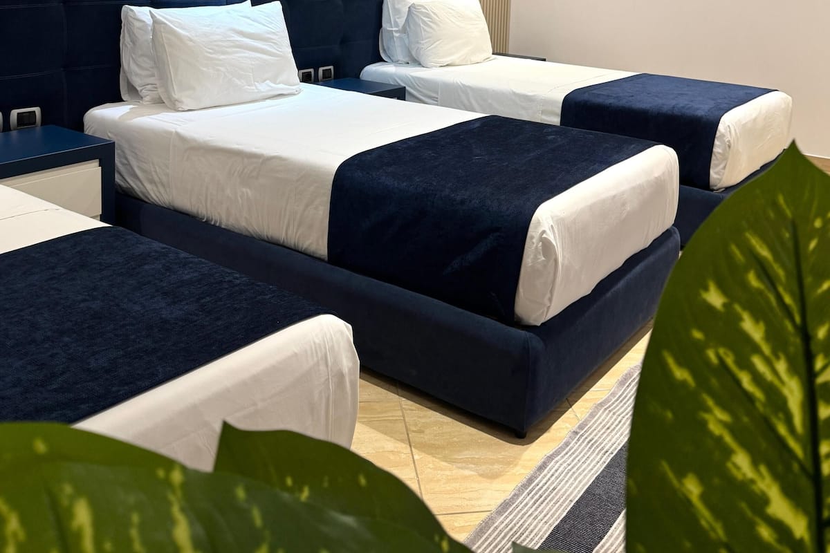 A modern hotel room with a large bed, two smaller beds, a desk, and a plant.