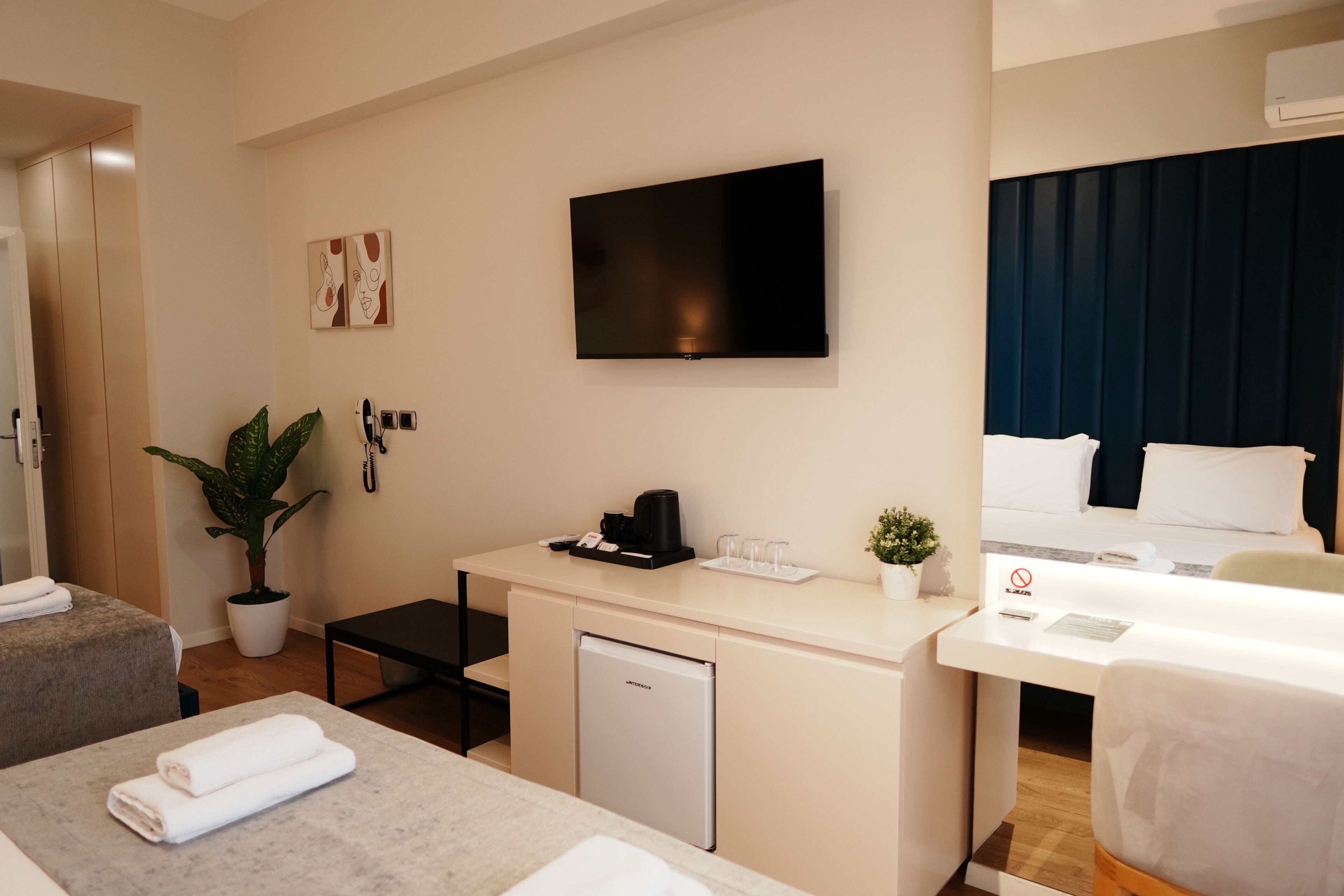 Une chambre d’hôtel avec un lit, un bureau avec une télévision, une petite plante et un mini-bar.