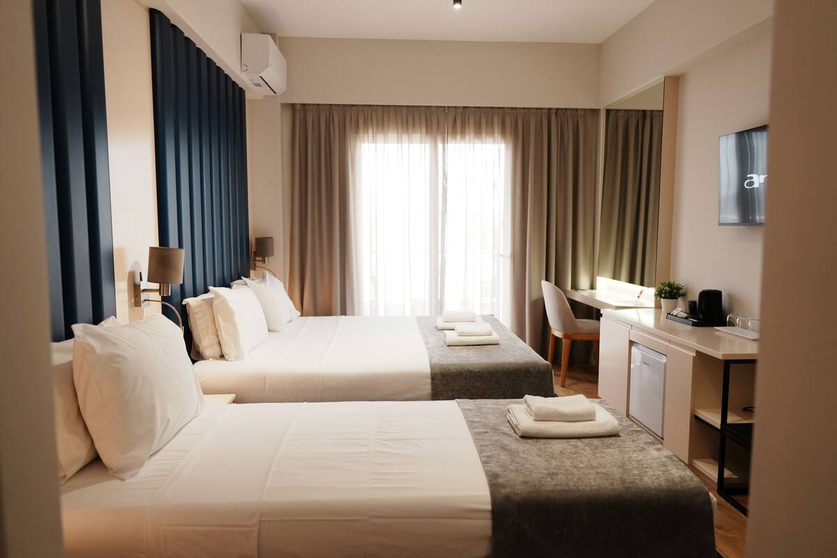 A hotel room with two beds, a desk, a chair, a TV, and a window with curtains.