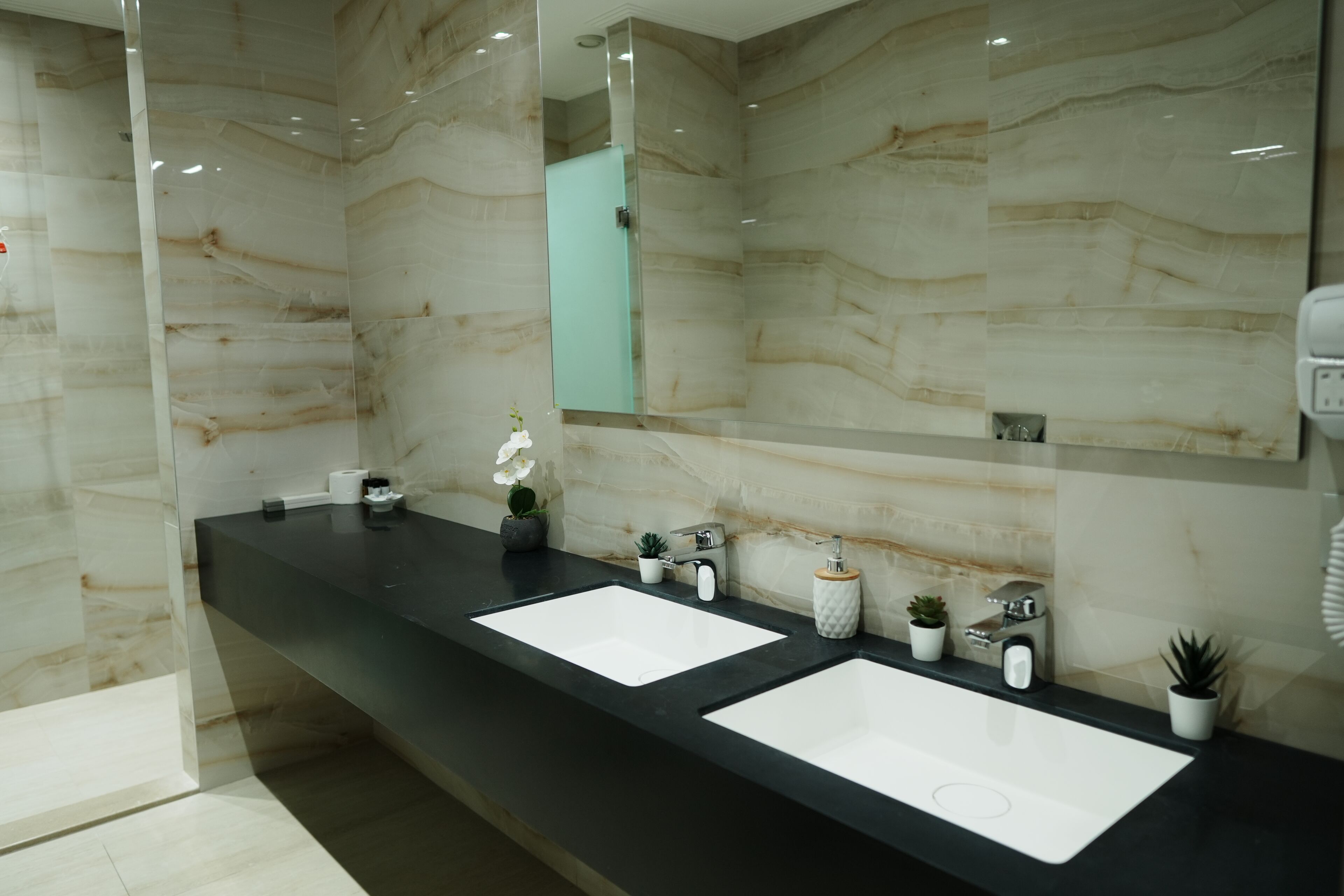 A modern bathroom with two sinks, marble walls, and a large mirror.