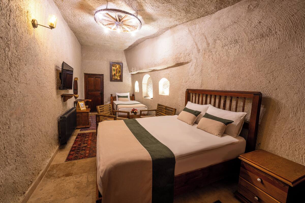 A bedroom with a large bed, a wooden nightstand, a dresser, a desk with a chair, and a small table with a lamp.
