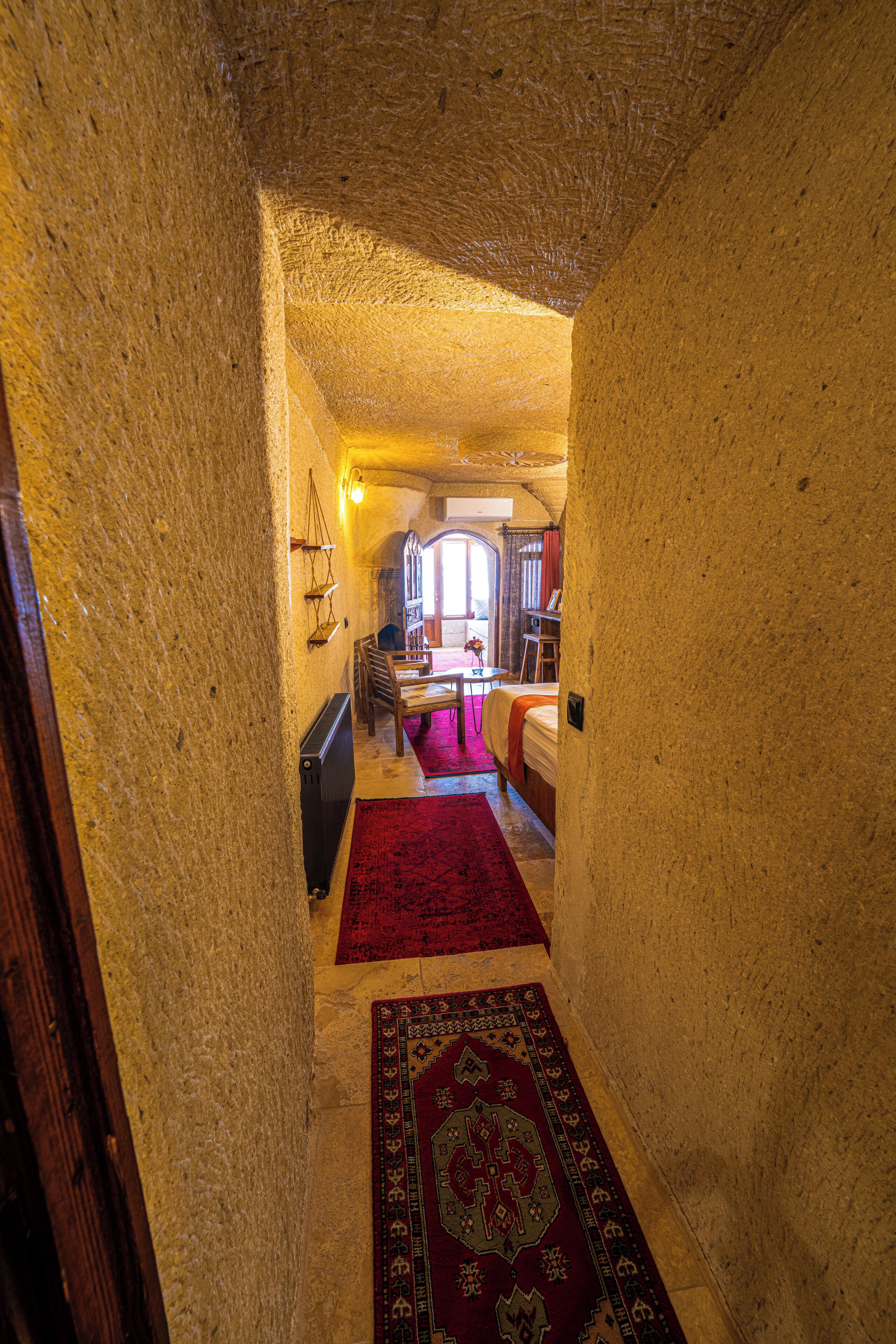 A narrow hallway with a red carpet leading to a bedroom with a bed and a window.