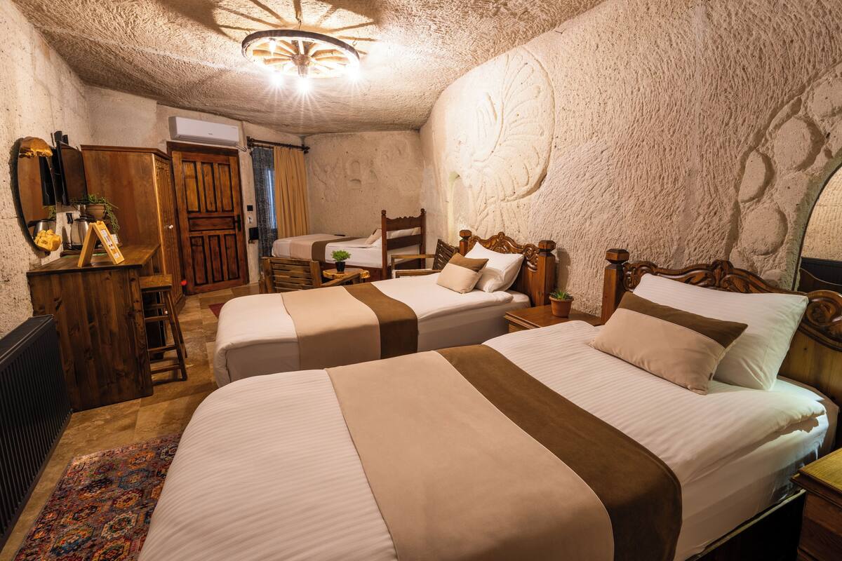 A room with two beds, wooden furniture, a small table with a plant, and a unique textured wall.