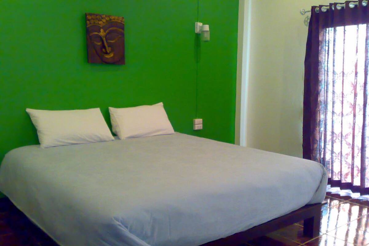 A bed with white linens in a room with green walls and a window with patterned curtains.