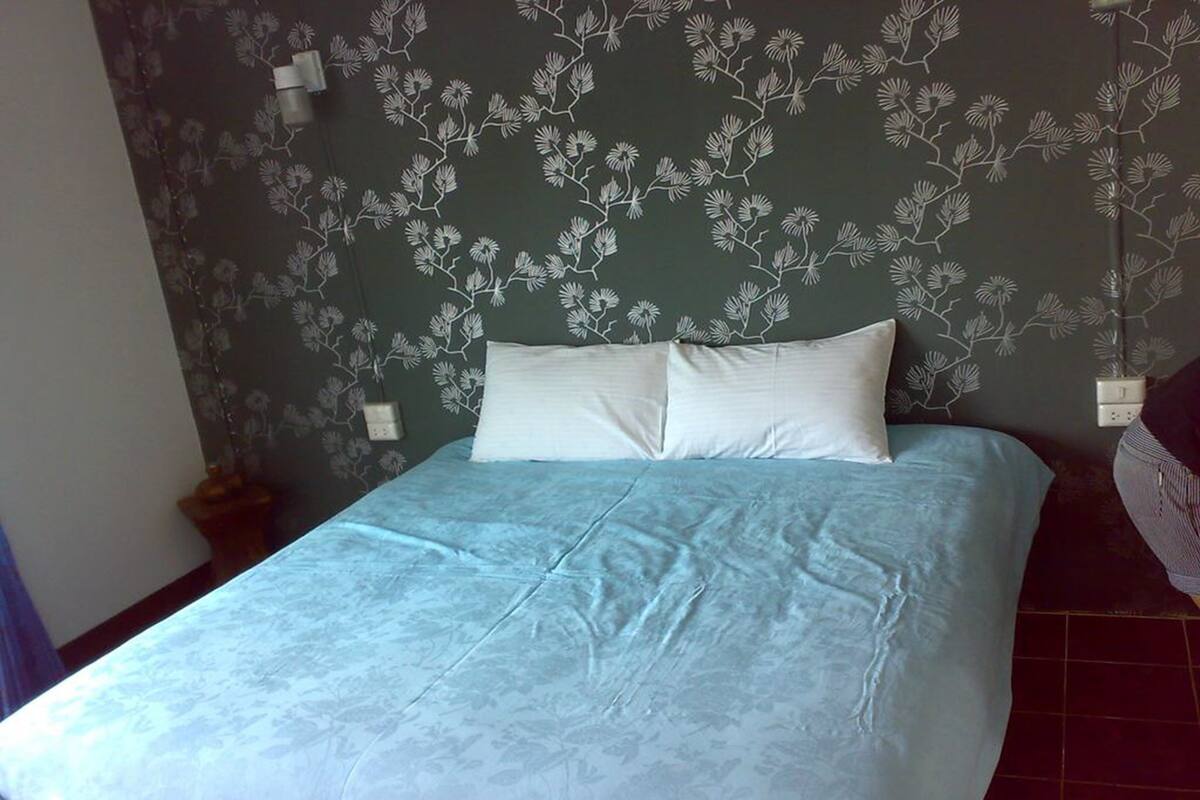 A bed with a floral-patterned headboard, a white pillow, and a blue bedspread.