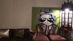 A room with a green wall, a large framed artwork, a wooden chair, a wooden table, and a traditional lamp. - Moon House at Clock Tower (Chiang Rai)