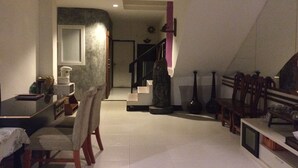A spacious living area with a dining table, chairs, a sofa, and a staircase leading to an upper level. - Moon House at Clock Tower (Chiang Rai)