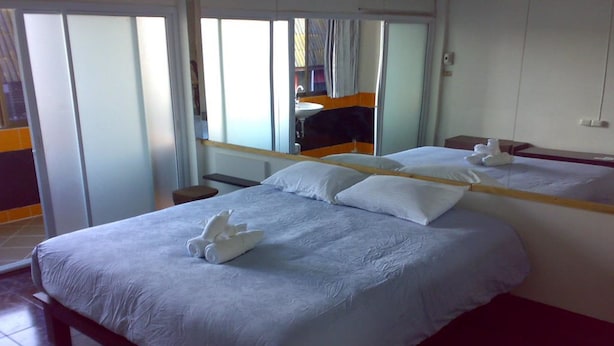 A hotel room with a large bed, a mirror, a small table, and a view of the outside. - Moon House at Clock Tower (Chiang Rai)