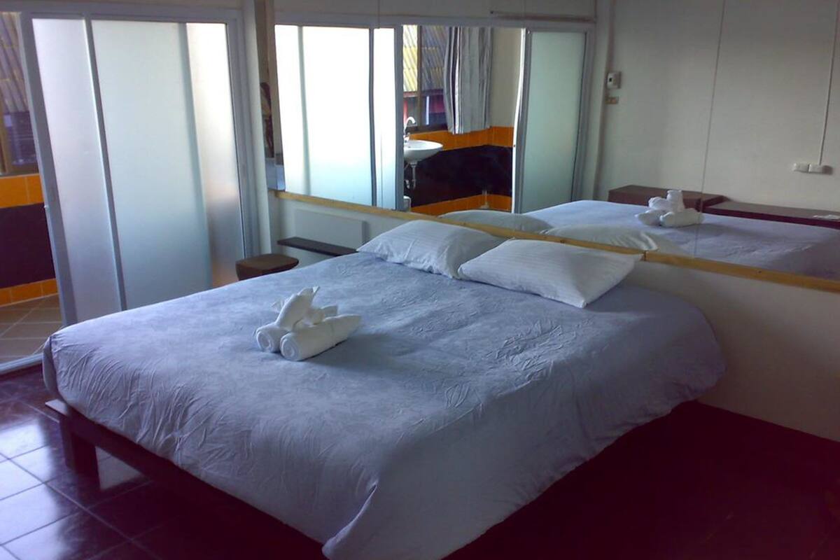 A hotel room with a large bed, a mirror, a small table, and a view of the outside.