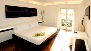 Een moderne hotelkamer met een groot bed, een klein tafeltje met een stoel, een schilderij aan de muur en een balkon met tuinmeubilair.