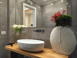 A modern bathroom with a large white vessel sink, a mirror, and a decorative leaf-shaped vase with red flowers. - Best Season (Reggio Calabria)