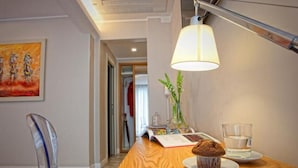 A modern hotel room with a wooden desk, a clear glass vase with flowers, a muffin on a plate, and a glass of water. - Best Season (Reggio Calabria)