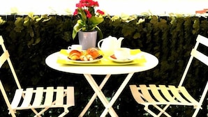 A round table with a yellow tablecloth, two white chairs, a potted plant with red flowers, and a plate with pastries and a teapot. - Best Season (Reggio Calabria)