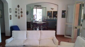 Een woonkamer met een witte bank, een salontafel en een eethoek op de achtergrond.