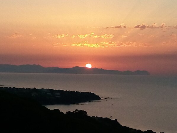 A sunset over a calm sea with distant land silhouettes. - In Cefalù, a relaxing villa surrounded by a green garden with a terrace overlooking the sea (Cefalù)