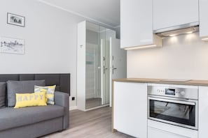 Eine moderne Küche mit Backofen und einem grauen Sofa, versehen mit einem Kissen mit der Aufschrift 'HAPPY'.