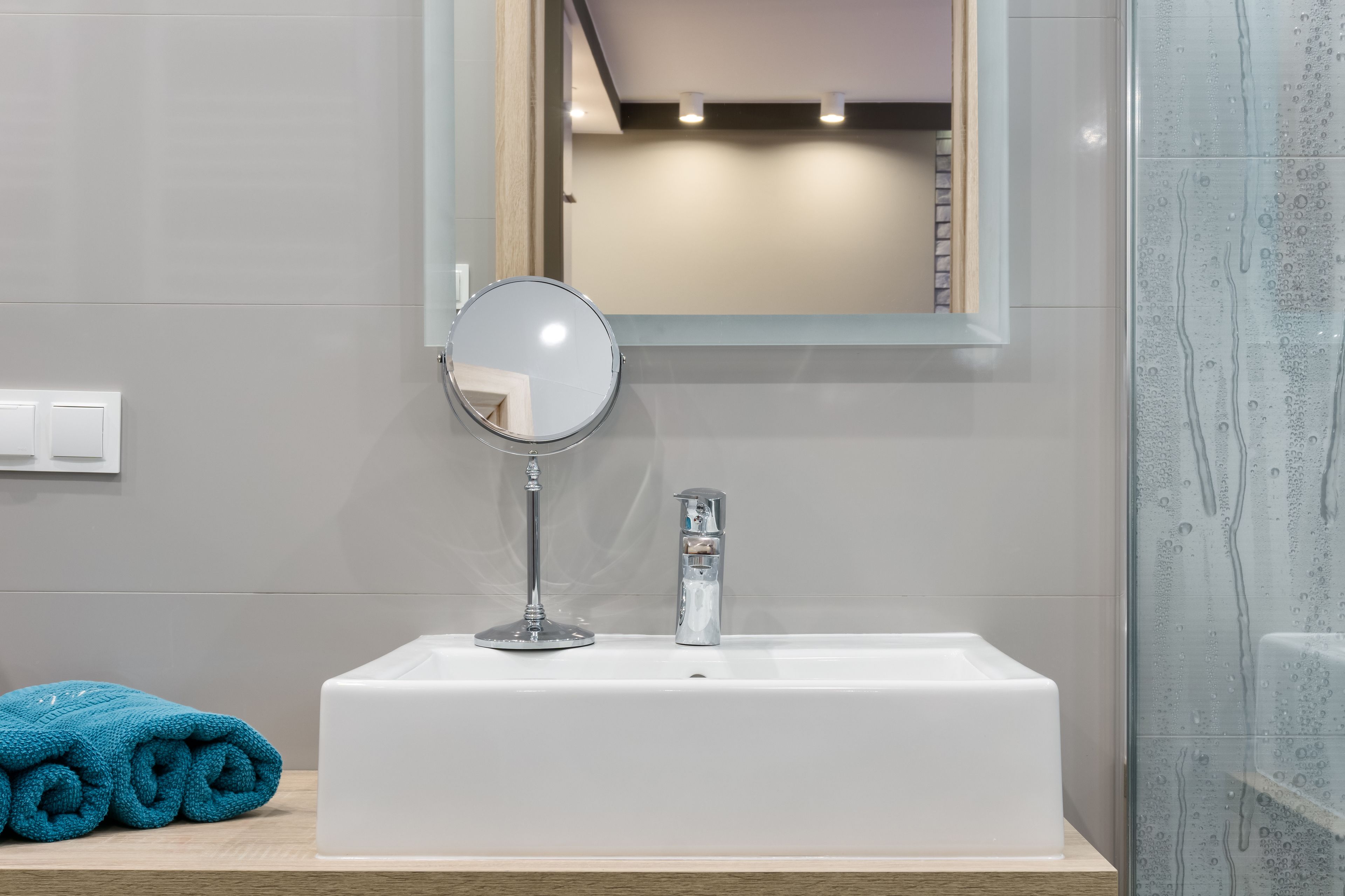 Un bagno con un lavandino bianco, uno specchio rotondo e un asciugamano sul ripiano.