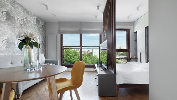 A modern hotel room with a balcony, a dining area, and a large window offering a view of the city. - Elite Apartments Spa Zone (Gdansk)