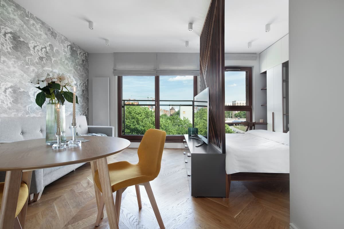 Habitación de hotel moderna con balcón, zona de comedor y un amplio ventanal con vistas a la ciudad.