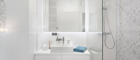 Un baño moderno con lavamanos, espejo y ducha blancos.