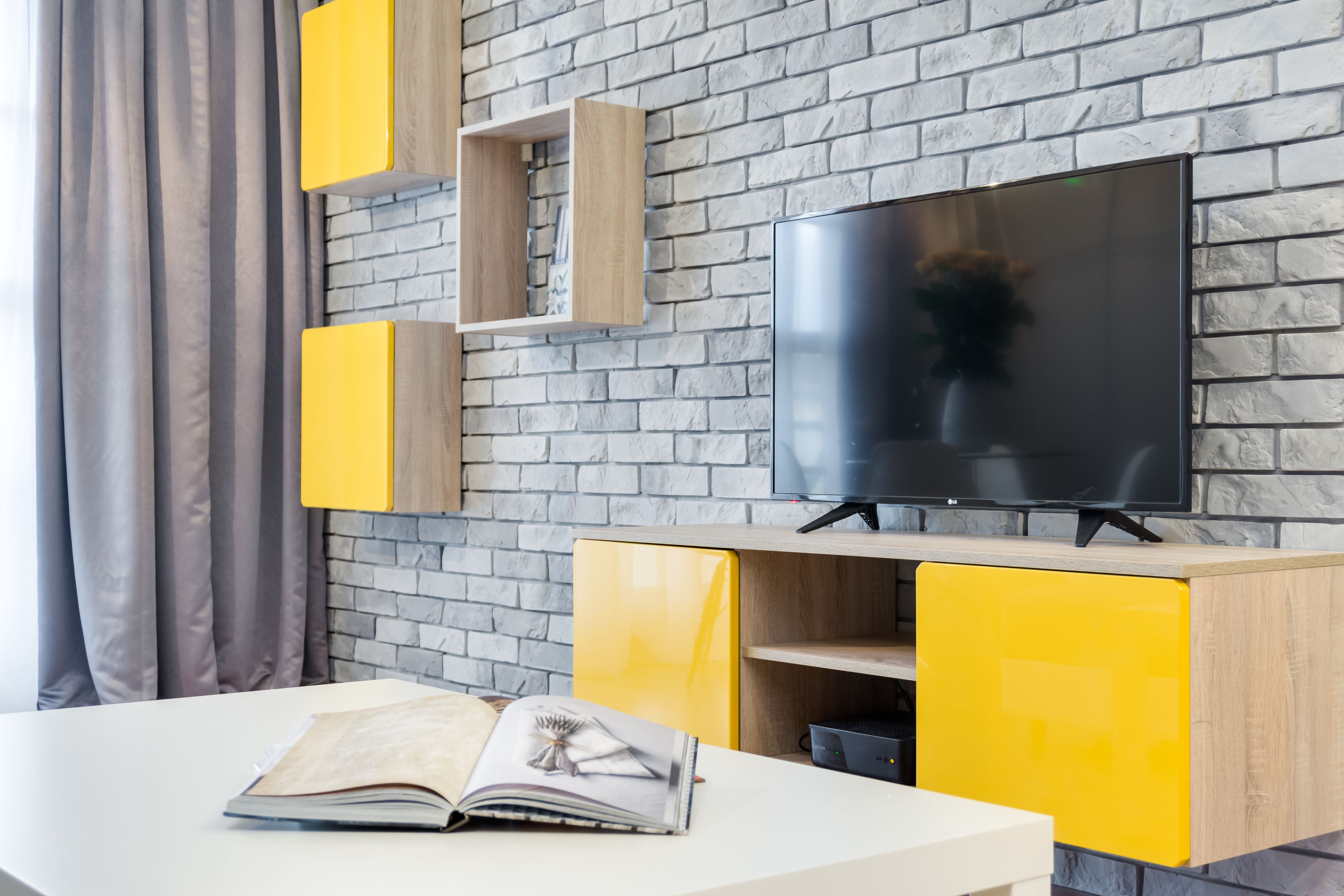 Ein modernes Wohnzimmer mit Backsteinwand, Flachbildfernseher und gelben Schränken.