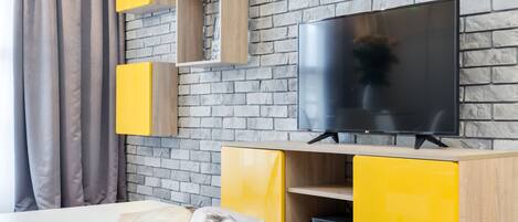 A modern living room with a brick wall, a flat-screen TV, and yellow cabinetry.
