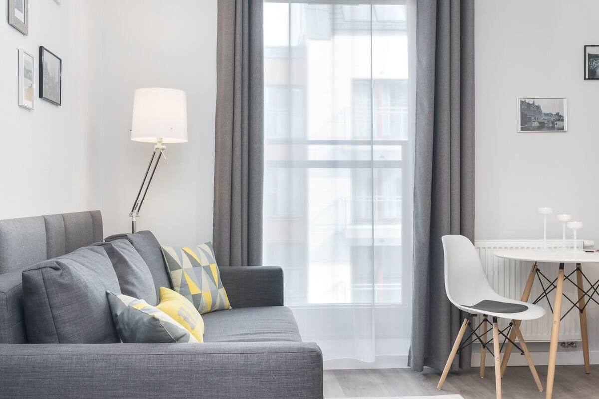 Una sala moderna con un sofá gris, una mesa blanca con una silla y una lámpara de pie.