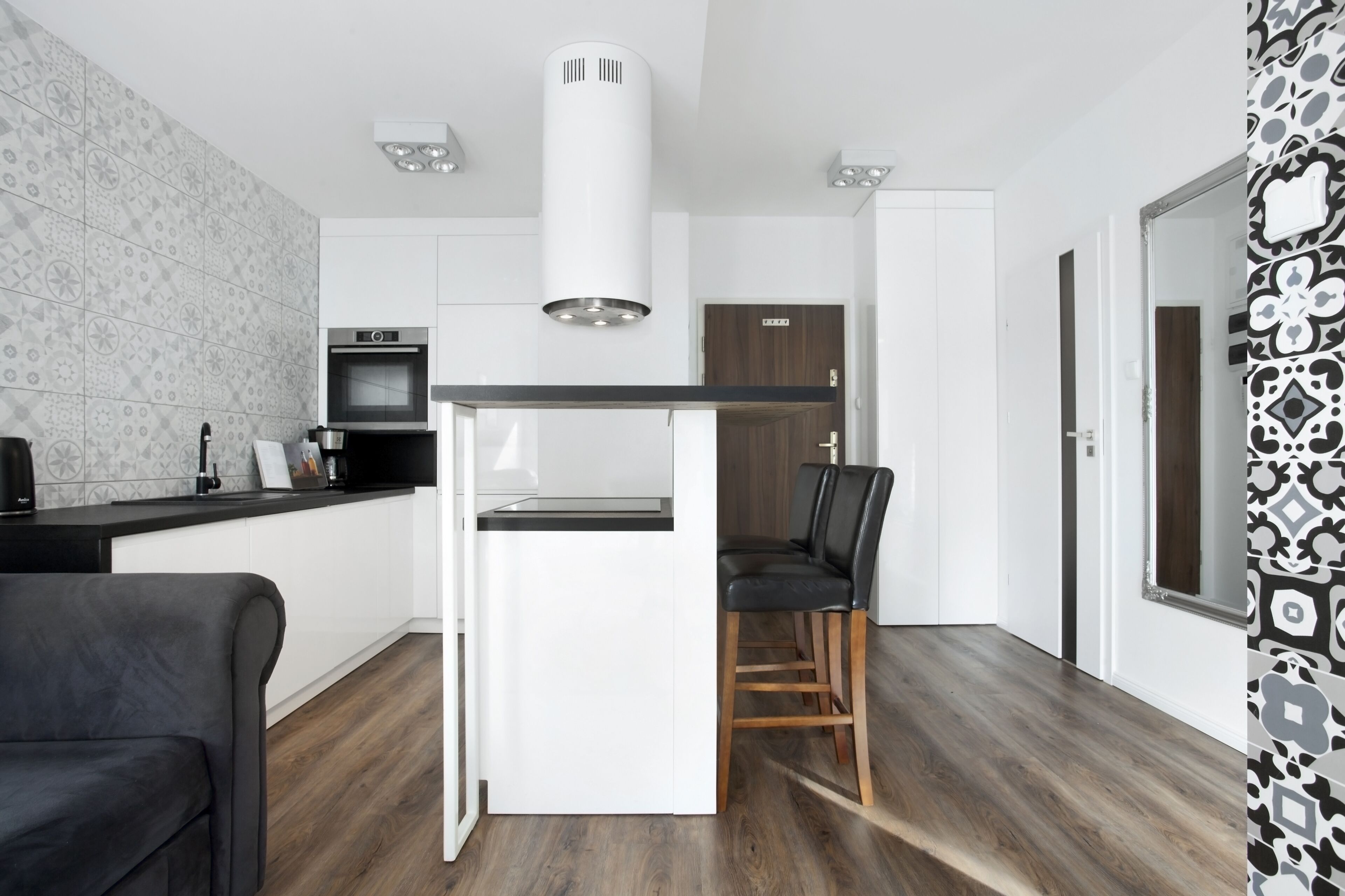 Une cuisine moderne avec des meubles blancs, un plan de travail noir, un four encastré et une chaise noire.