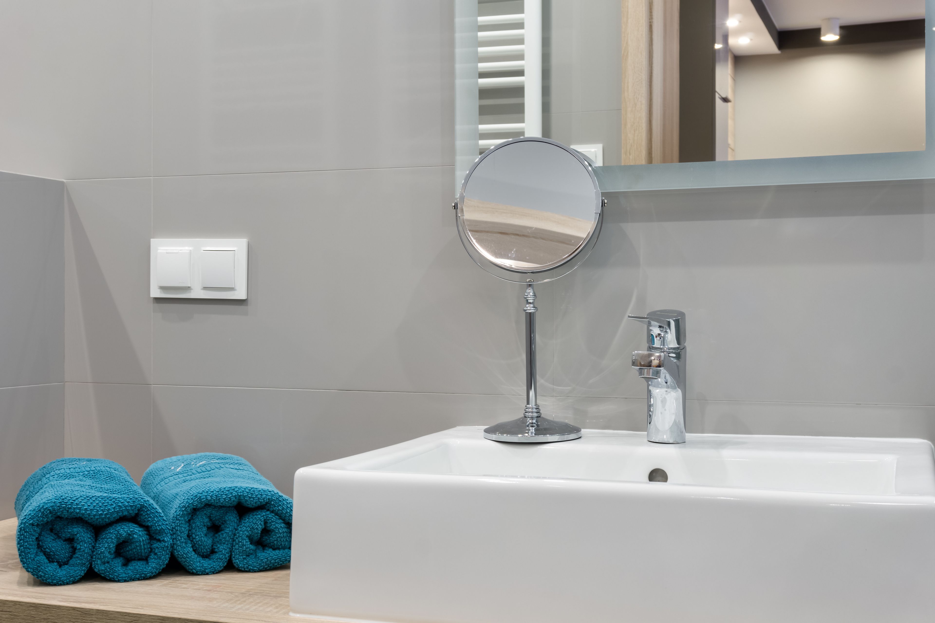 Een badkamer met een witte wasbak, een ronde spiegel en twee opgerolde handdoeken op een houten oppervlak.