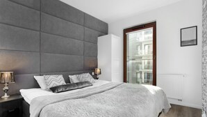 A modern bedroom with a large bed, grey headboard, and a view of a building through a glass door. - Elite Apartments Spa Zone (Gdansk)