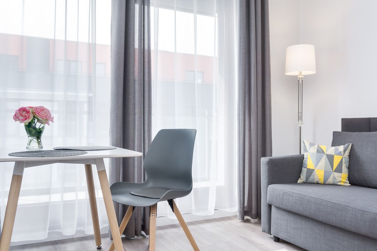 Une pièce moderne avec un canapé gris, une petite table sur laquelle est posé un vase de fleurs et une lampe.