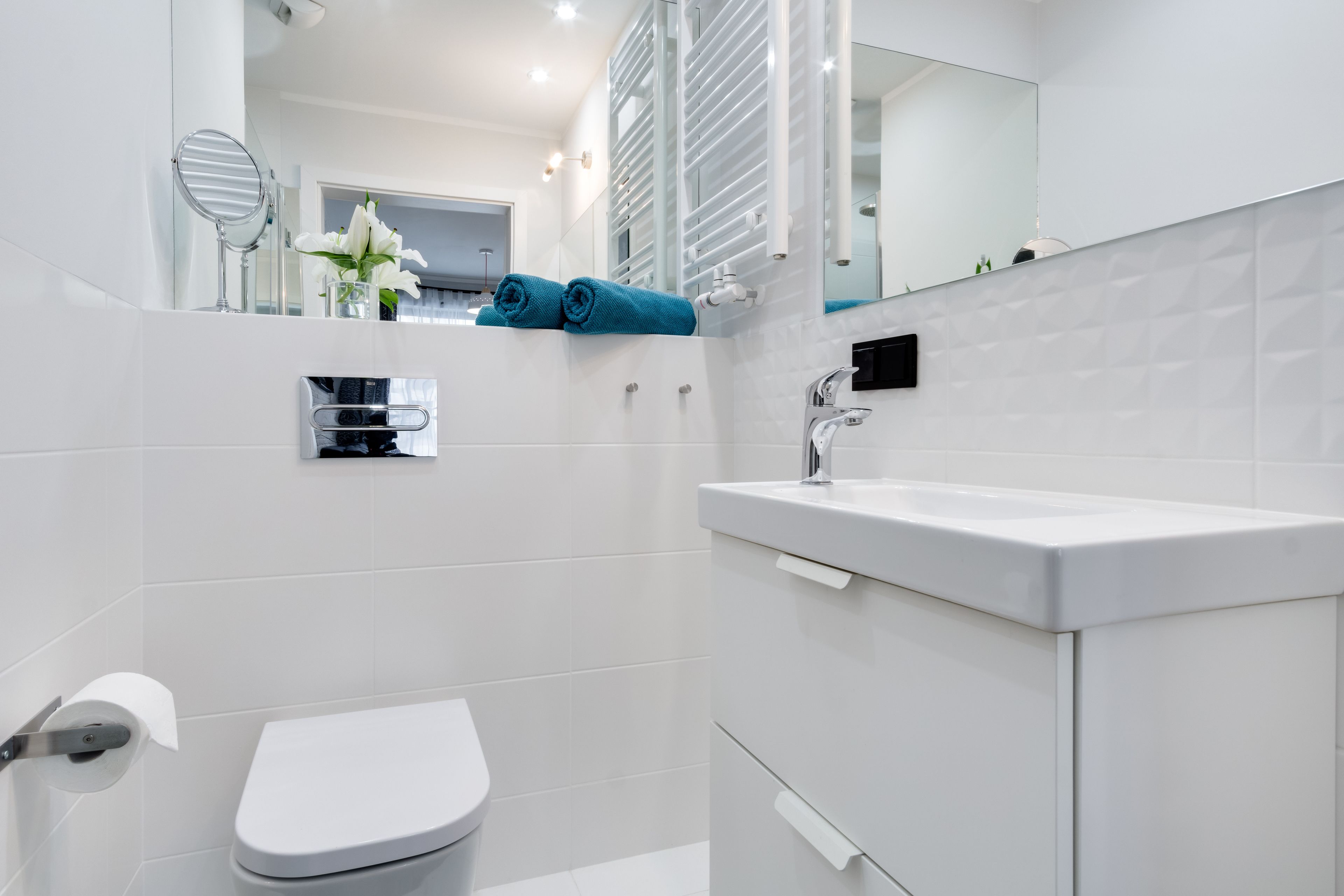 Uma casa de banho moderna com sanita branca, lavatório com espelho e um porta-toalhas.