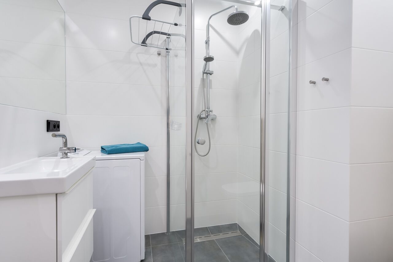 Ein modernes Badezimmer mit einer Duschkabine aus Glas, einem weißen Waschbecken und einem kleinen, weißen Schrank.