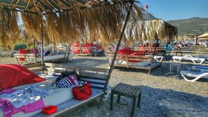 Een strand met ligbedden en parasols, een houten bankje en een kleine tafel.