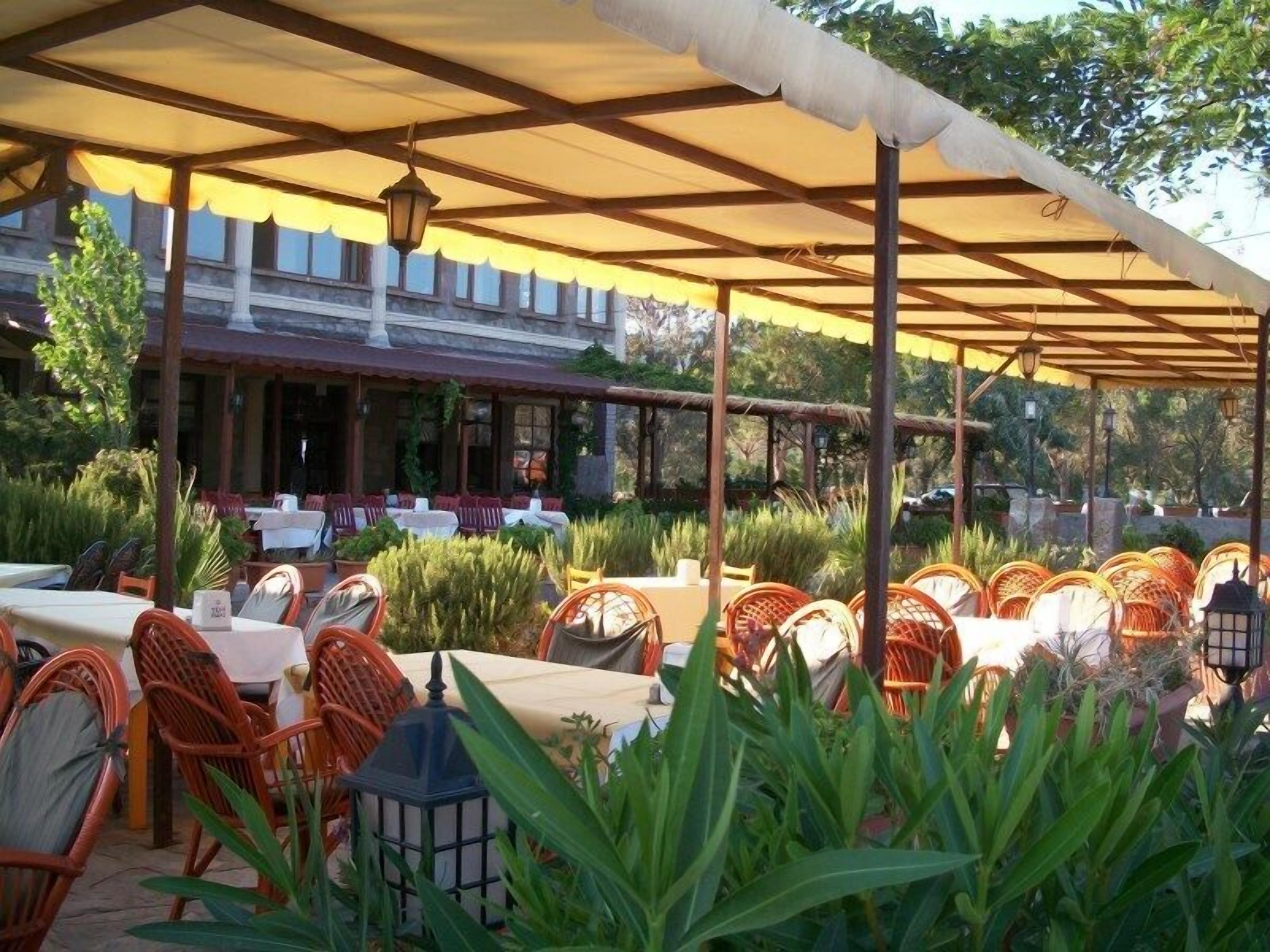 An outdoor patio with wicker chairs and tables, covered by a canopy, and surrounded by greenery.