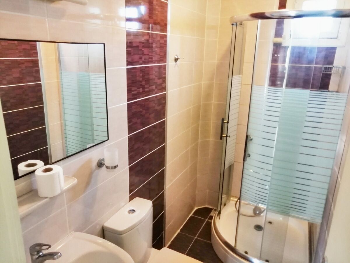 Un baño con inodoro, lavamanos, espejo y cabina de ducha de vidrio.