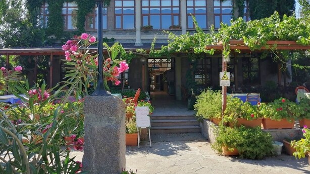 Een gebouw met een overdekte ingang, potplanten en een bord waarop een restaurant aangegeven staat.