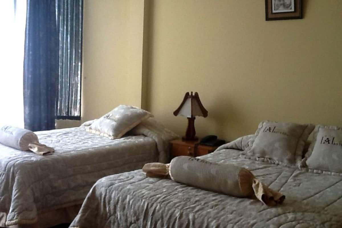 A hotel room with two beds, a nightstand with a lamp, a framed picture on the wall, and a window with curtains.