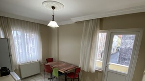 A compact kitchen with a dining table and chairs, a window with curtains, and a radiator. - Menekse Apart (Trabzon)