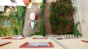 An aerial view of a residential area with a paved patio, a small garden, and a building with a red roof. - Menekse Apart (Trabzon)