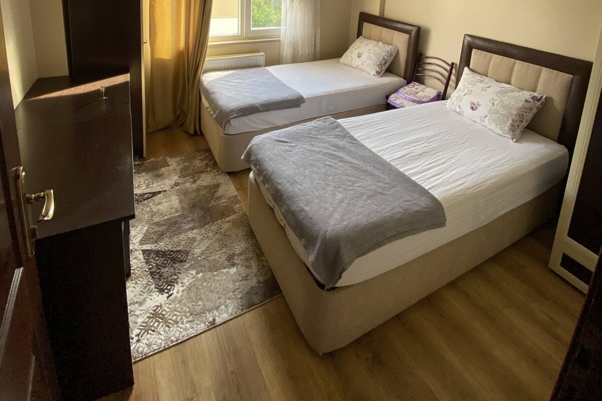 Hotellihuone, jossa on kaksi sänkyä, vaatekaappi, kattotuuletin ja ikkuna, jossa on verhot.